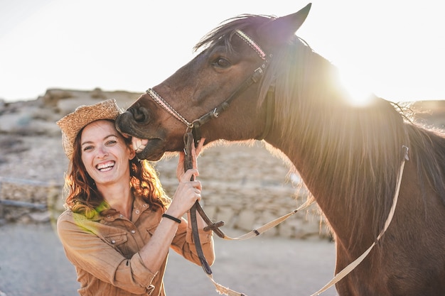 Young farmer woman playing with her horse in a sunny day inside corral ranch - Concept about love between people and animals - Focus on girl face