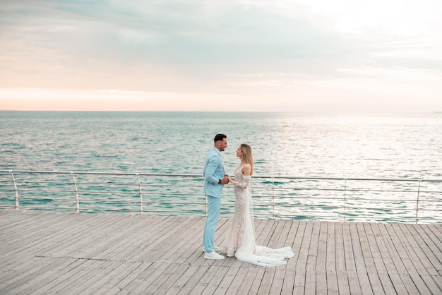 Young fashion couple holding hands on the wooden bridge in background of the sea and blue sky