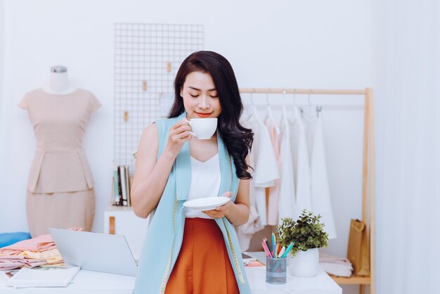 Young fashion designer on her atelier making a pause and drinking coffee