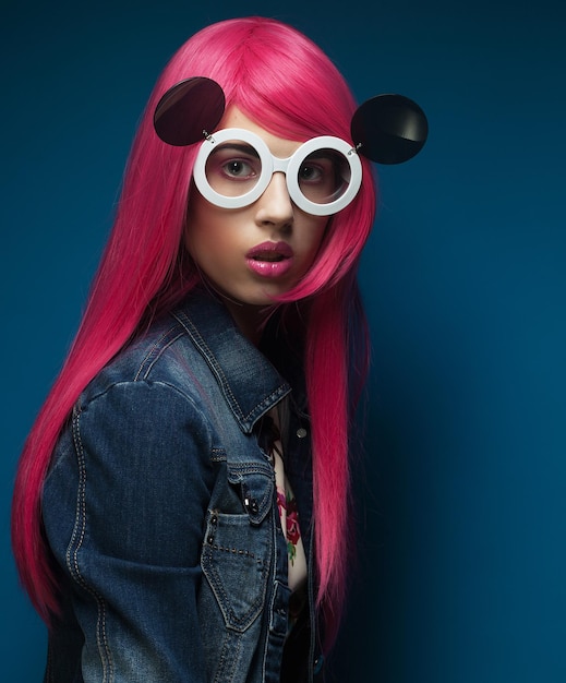 Young fashion girl with pink hair and big sunglasses over blue background