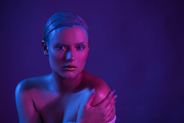 Young fashion model with bright makeup on a purple background with bare shoulders.