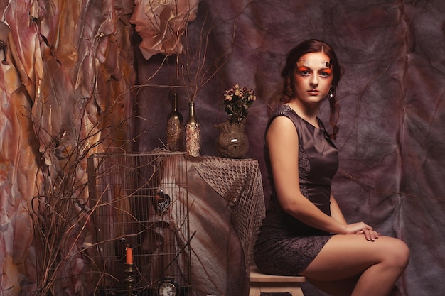 Young fashion model with creative make up sitting on a stool