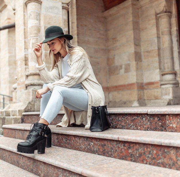 Photo young fashion woman in trendy stylish clothes sits on steps in urban architecture lifestyle street fashion