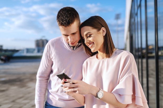 Young fashionable couple standing on balcony and looking at smart phone