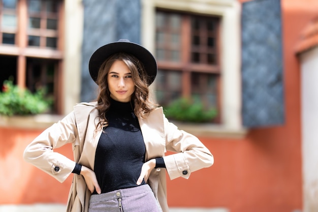 Young fashionable woman in hat and coat posing in street.