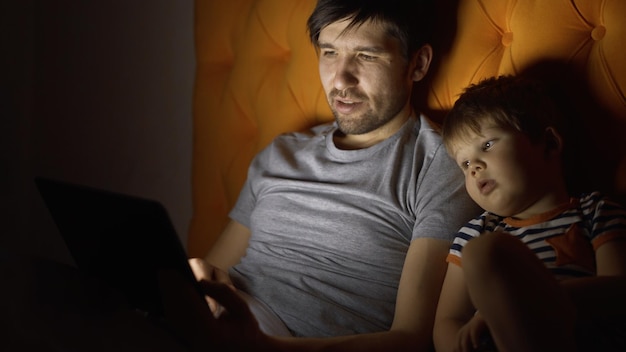 Young father and his little son watching cartoon movie using tablet computer