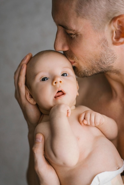 A young father holds his newborn son in a diaper in his arms and kisses him