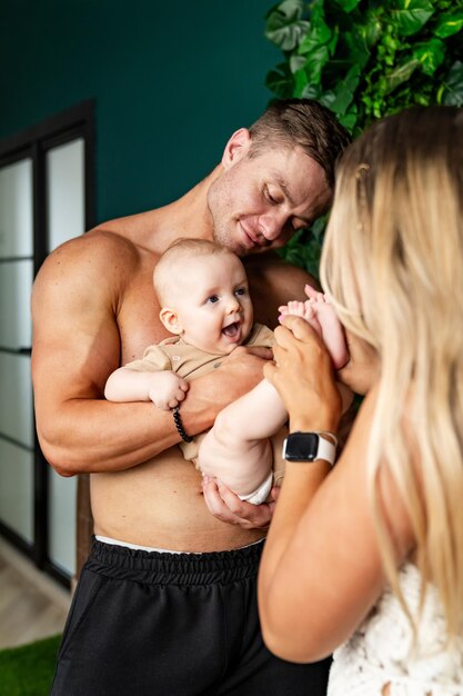 Young father and mother are holding their baby in their arms and smiling at each other