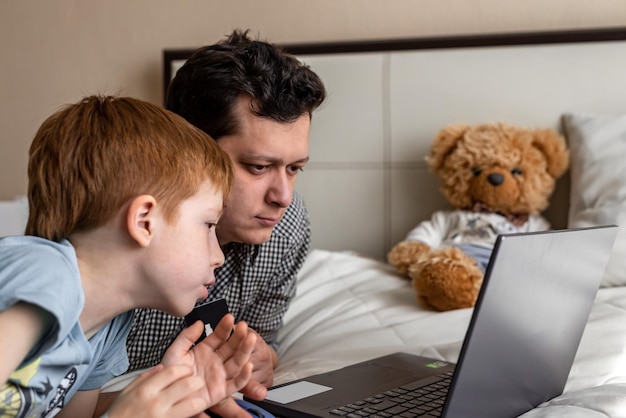 Young father and son shopping online together family time Child redhaired boy and dad at the laptop choose purchases