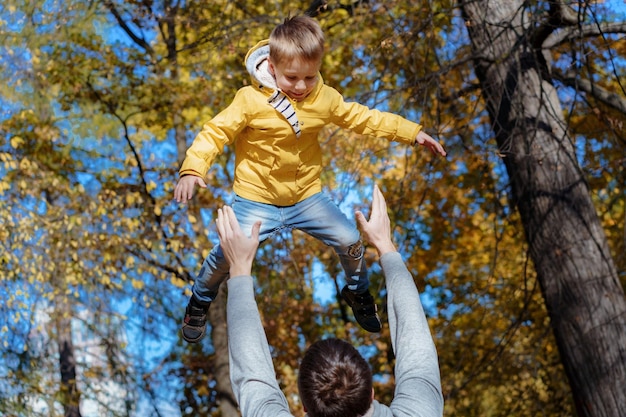 Young father throws up his cute and little son in the air in autumn park