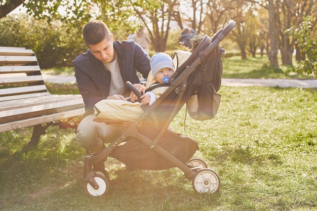 A young father on a walk with a stroller and a baby in an autumn park