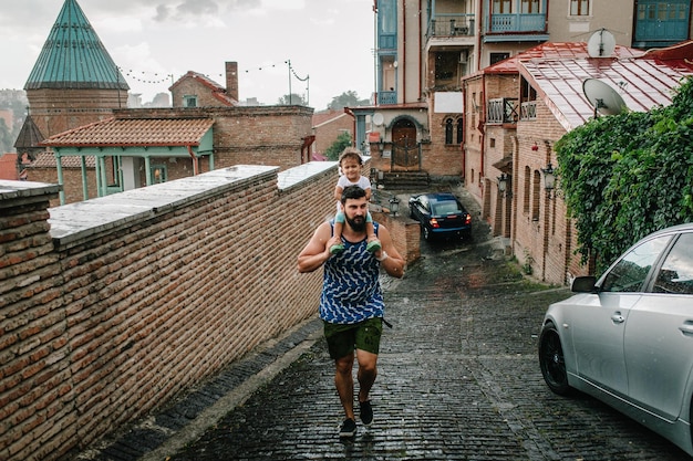 Young father walking with little daughter outdoors on streets in old town of Tbilisi in the capital of Georgia on rainy day Dad and girl running away in the rain in the city