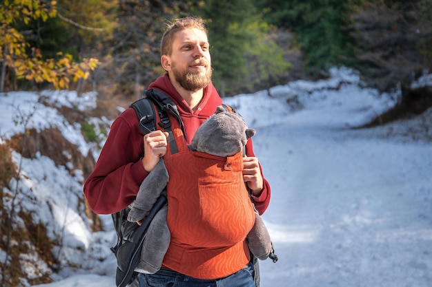 Photo young father with his baby boy in ergonomic baby carrier in winter forest