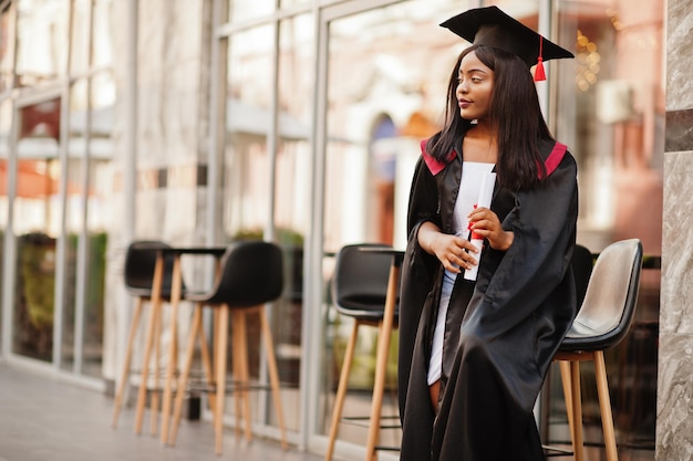 Young female african american student with diploma poses outdoors.