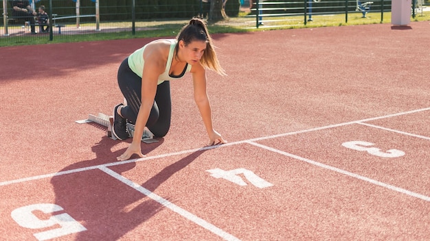 Young female athlete beyond start line assuming crouching start position and running along a stadium