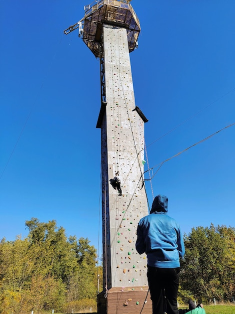 A young female athlete climbs a climbing wall A boy holds her up by a rope