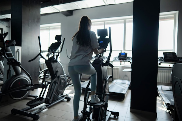 Young Female Athlete Exercising on Elliptical Trainer in a Gym view from the back