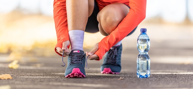 Young female athlete tying shoelaces before running in autumn park a bottle of water was leading her Close up