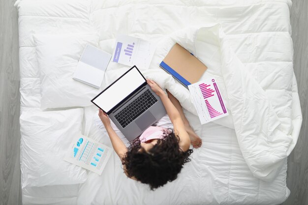 Young female in bed with laptop prepare annual report from home