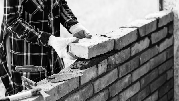 Photo a young female bricklayer builds a wall puts a brick on a cement mortar