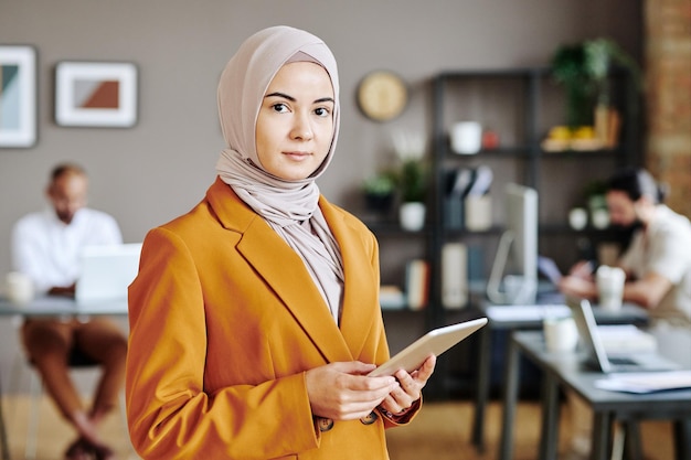 Young female business leader in hijab with tablet in hands looking at camera