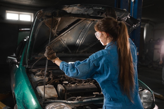 Young female car repair worker A female mechanic checks the oil level in the car's engine A mechanic checks and maintains a car engine or vehicle on his own