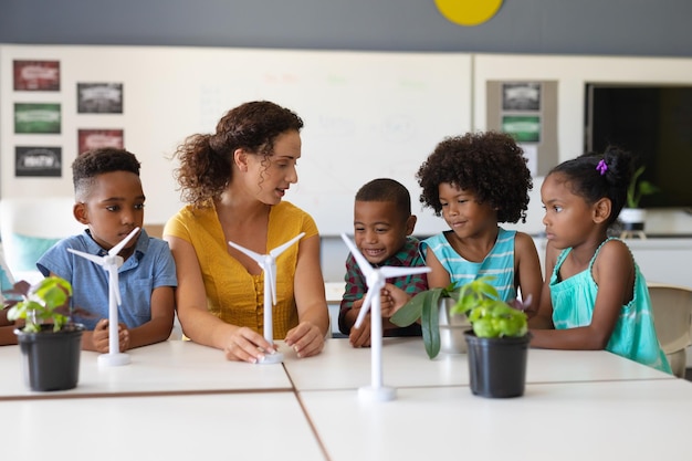 Young female caucasian teacher showing windmill model to african american elementary students