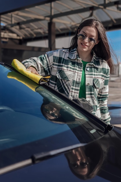 A young female cleaning and polishing her car with yellow microfiber cloth Concept of car taking care