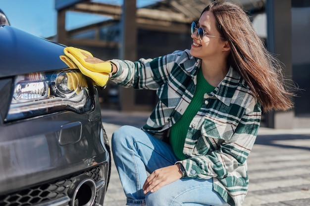 A young female cleaning and polishing her car with yellow microfiber cloth Concept of car taking care