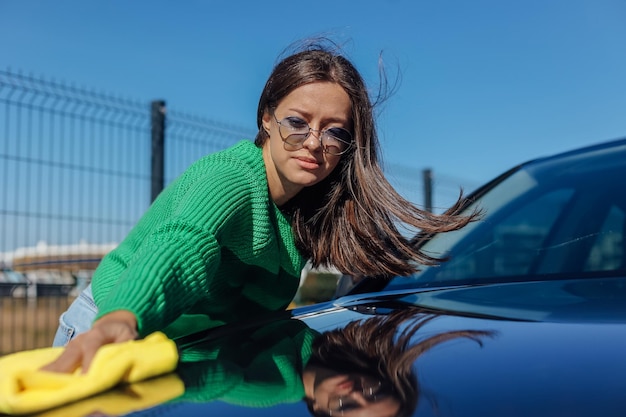 A young female cleaning and polishing her car with yellow microfiber cloth Concept of car taking care