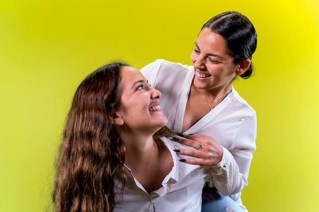 Young female couple hugging yellow background