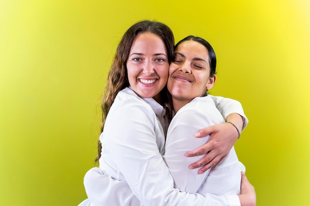 Young female couple hugging yellow background