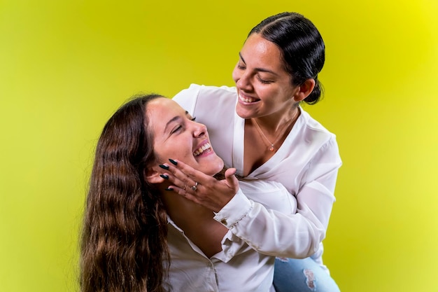 Young female couple piggyback yellow background