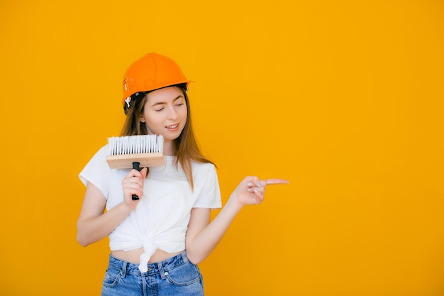 Young female decorator with paint roller on yellow background