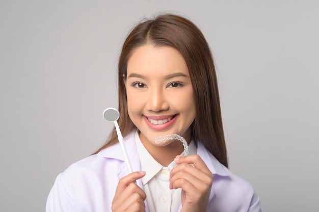 Young female dentist holding invisalign braces over white background