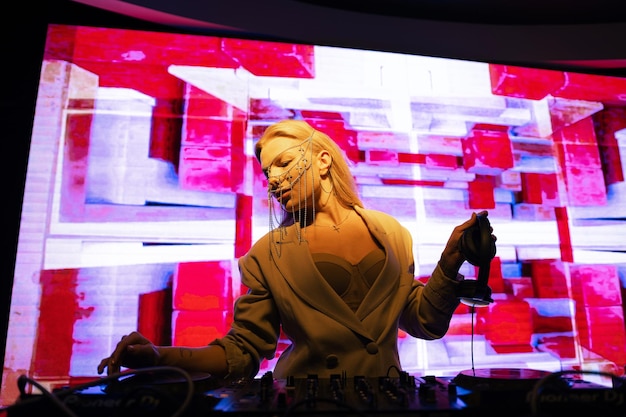 Young female DJ in a nightclub at the console the girl is wearing a white suit and jewelry on her face