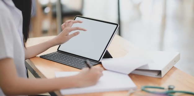 Young female doctor examining the patient chart with digital tablet and writing down on document 