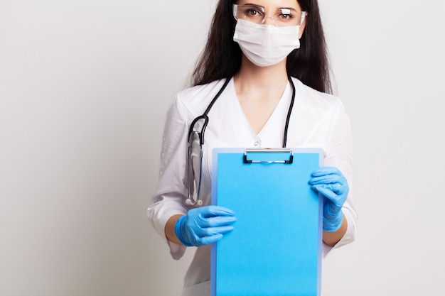 Young female doctor in a mask holds a blank sheet of paper