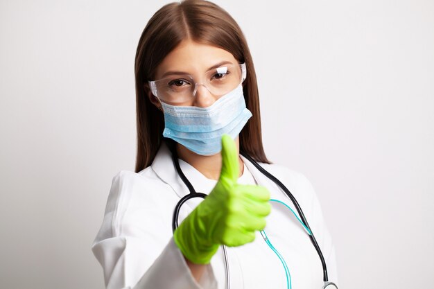 Young female doctor in a mask holds a thumb up