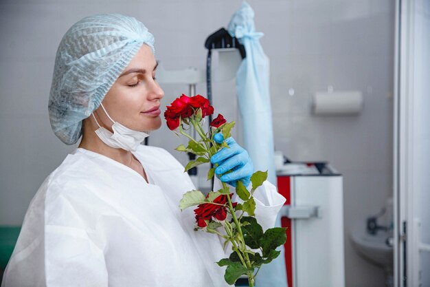 A young female doctor in a white protective suit cap and gloves holds a red rose presented to her