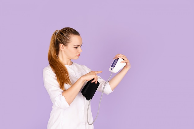 Young female doctor in white uniform with phonendoscope on her neck holding tonometr 