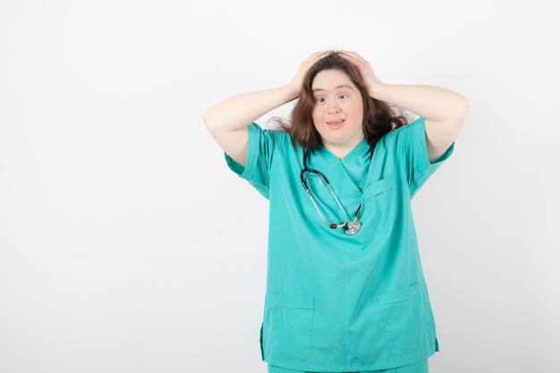 Young female doctor with down syndrome standing on white.