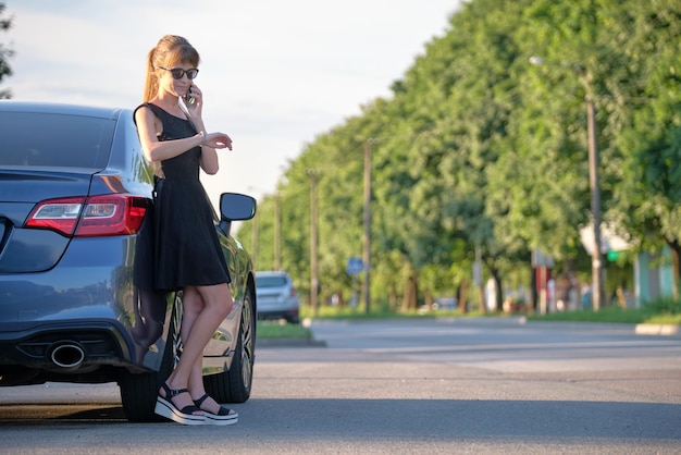 Young female driver standing near her car talking on mobile phone on a city street in summer