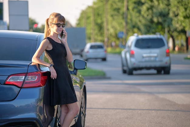 Young female driver standing near her car talking on mobile phone on a city street in summer