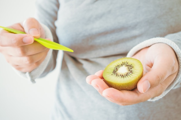 Young female eating ripe kiwi fruit with wooden spoon