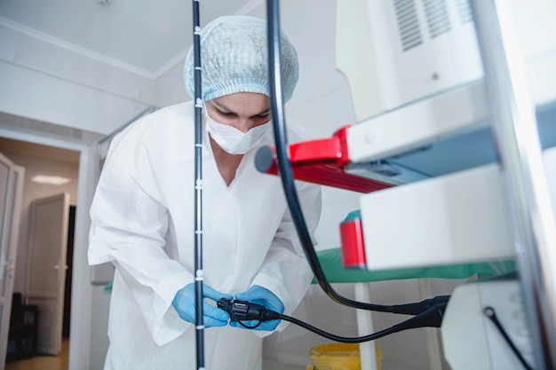 A young female endoscopist in a white protective suit cap and gloves prepares the equipment for work