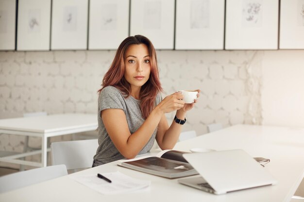 Photo young female entrepreneur taking a job break sitting in an open space hub or coworking drinking coffee looking at camera