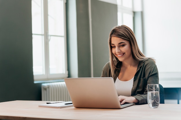 Young female entrepreneur working while sitting at a desk, typing on her laptop computer in a office.