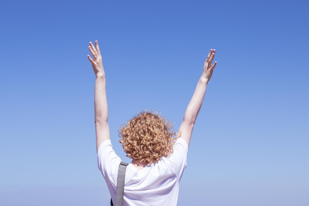 Young female european tourist back view raised hand curly blond hair Sky copy space