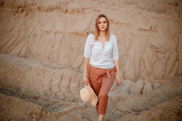 Young female exploring sandy beach with hat. Hipster girl, young traveler in nature desert. A woman walks in the desert to meet. Woman walks.